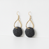 A pair of gold and black dangle earrings on a clean white background. Each earring features a gold teardrop-shaped wire frame suspending a round, textured black disc with a floral petal pattern.