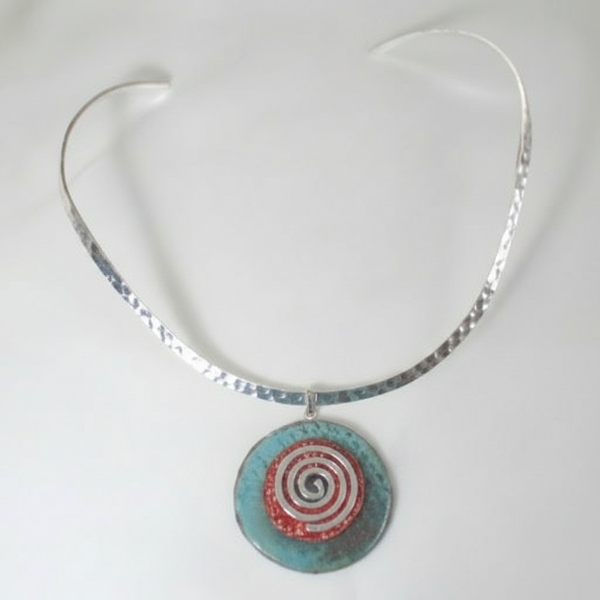A silver-toned open-cuff necklace featuring a circular turquoise pendant with a red and white spiral design, shown against a plain white background.