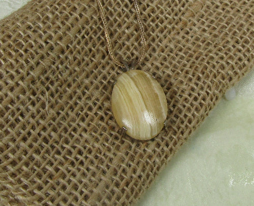 A natural wood oval pendant necklace with a gold-toned chain, displayed on a textured burlap surface.