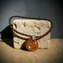 A handmade pendant necklace with a brown and black leopard print cord and a round, glossy orange-brown glass pendant with wavy lines and small dots, displayed on a textured stone block.
