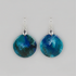 A pair of round drop earrings with a marbled blue and teal stone-like pattern, suspended from silver fishhook wires, shown against a solid gray background.