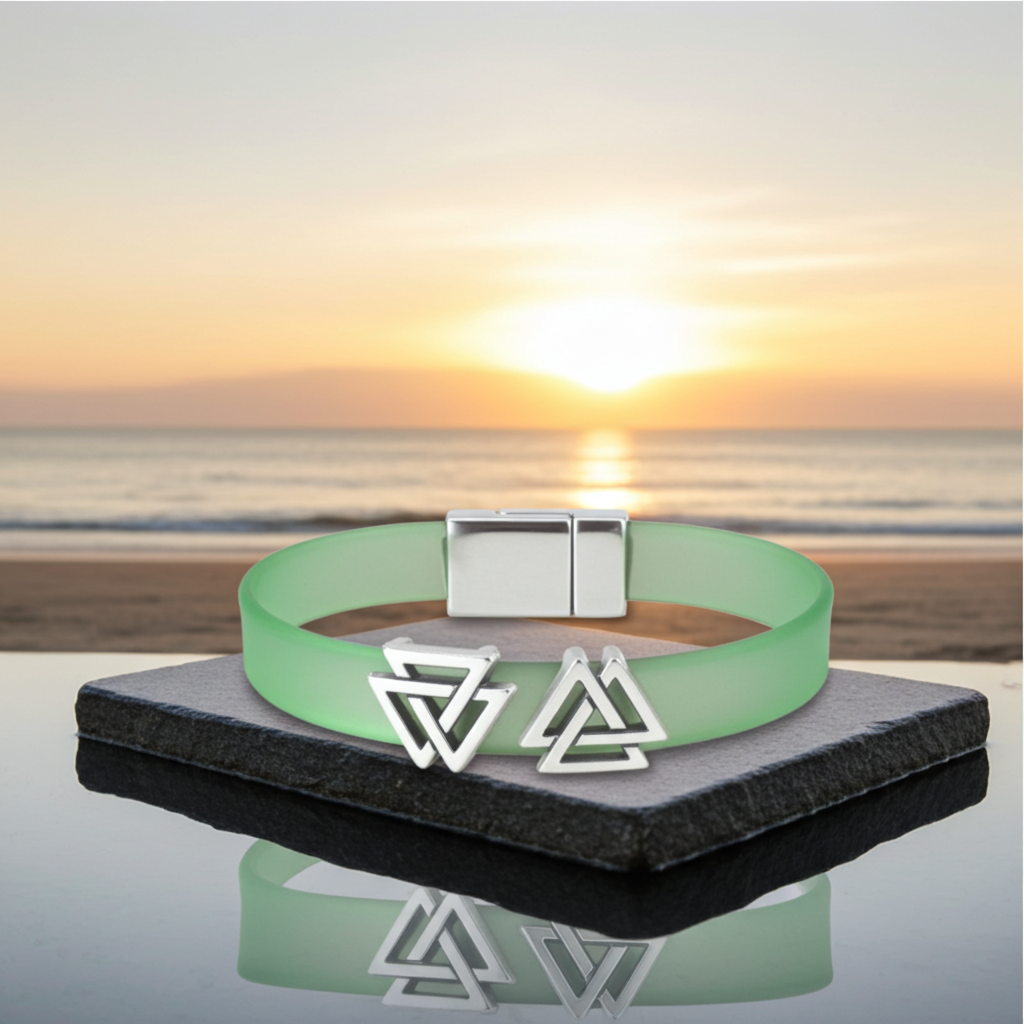 A light green silicone bracelet with a silver magnetic clasp and two interlocking triangle charms, displayed on a dark stone block with a beach sunset background.