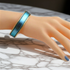 A close-up of a mannequin hand wearing a wide metallic bangle bracelet with a blue gradient center and gold-toned edges, resting on a white marble surface.