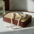 Pearl necklace on a jewelry box with a bottle of perfume in the background