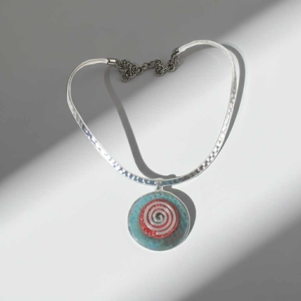 A silver-toned hammered cable bracelet with a circular pendant featuring a red, white, and turquoise spiral design, shown on a white background with dramatic diagonal shadows.