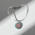 A silver-toned hammered cable bracelet with a circular pendant featuring a red, white, and turquoise spiral design, shown on a white background with dramatic diagonal shadows.
