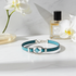Blue bracelet with silver clasp on a white surface with flowers and a perfume bottle in the background
