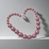 A heart-shaped beaded necklace made of glossy, rounded dusty pink beads with a small silver heart charm, displayed on a light gray surface.