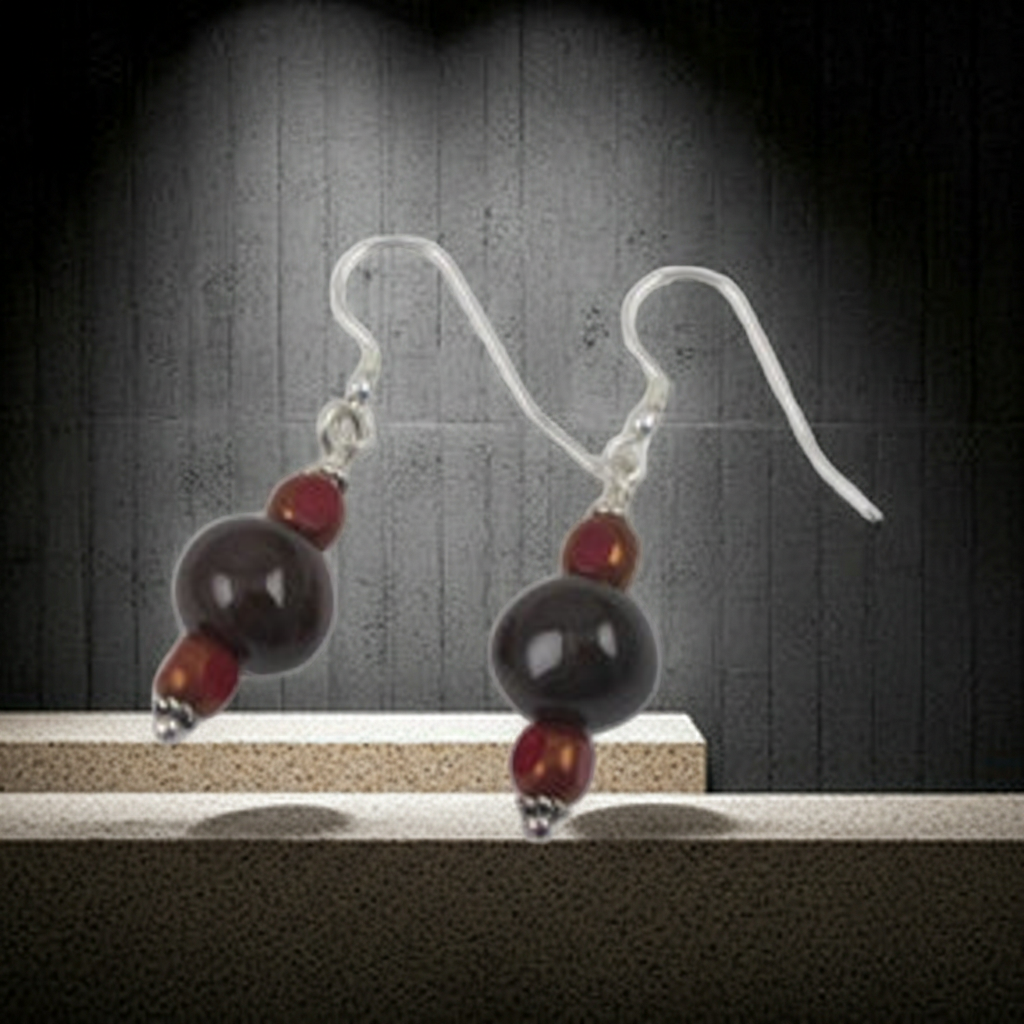 A pair of dangling earrings with clear fishhook wires, a small red bead, a larger dark brown bead, and a smaller red bead, displayed on a light surface against a dark textured background.