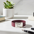 A burgundy leather bracelet with a polished silver-tone geometric buckle, displayed on a white marble desk next to a potted succulent.