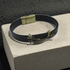 A black leather bracelet with an antique bronze dragon charm and matching clasp, displayed on a textured light gray stone block against a dark gray background.